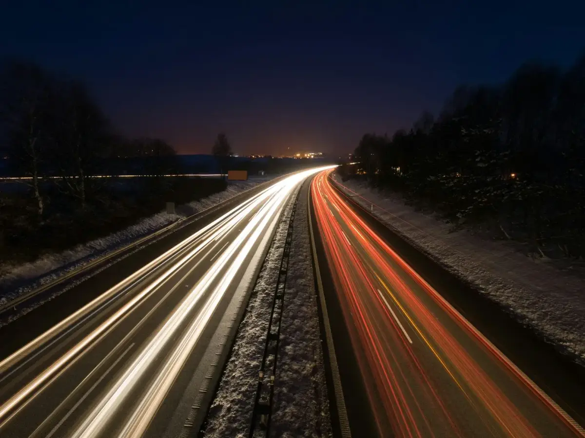 Long-exposure photograph of red and white light trails from truck and car traffic streaming along a highway at night
