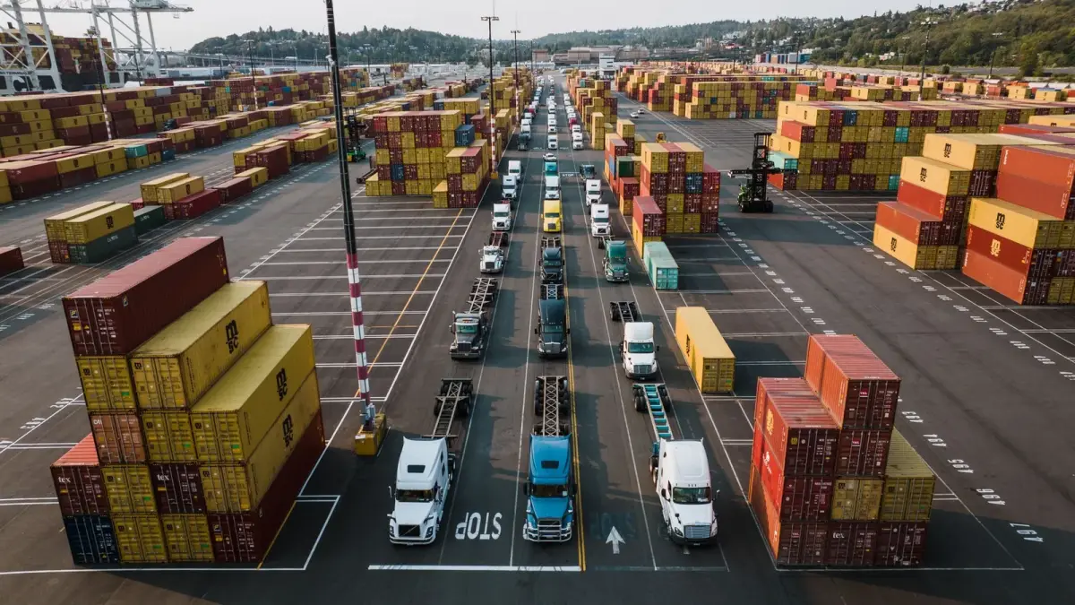 Aerial view of a busy container port, with trucks lined up in the lanes between rows of stacked shipping containers